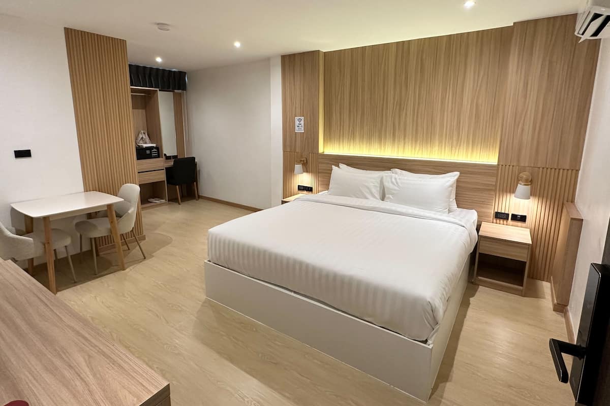 A hotel room with a large bed, a desk, and a chair. There is a wooden panel wall and a nightstand with a lamp.