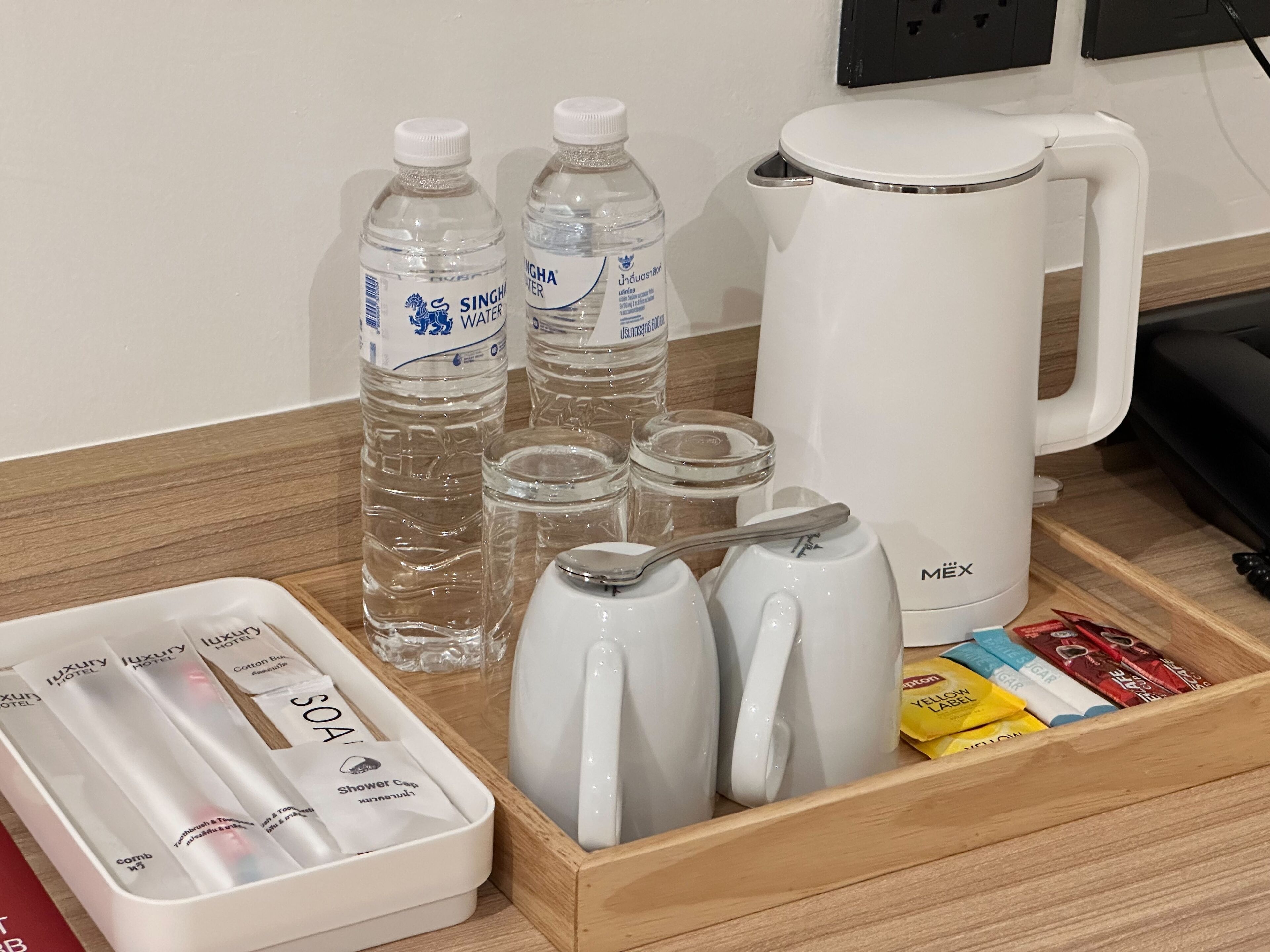 Cesto con servizi in camera contenente acqua in bottiglia, un bollitore elettrico bianco, un teiera e articoli da toilette.
