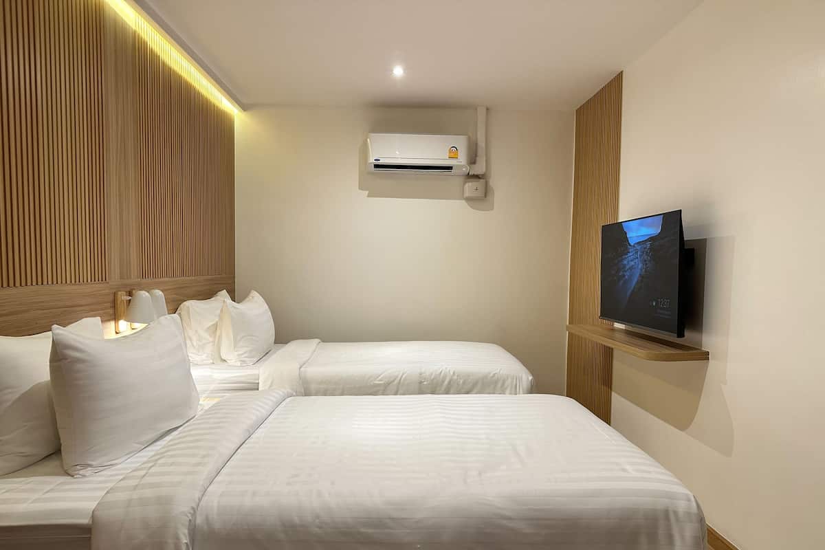 A hotel room with two beds, a flat-screen TV, an air conditioning unit, and a wooden panel wall.