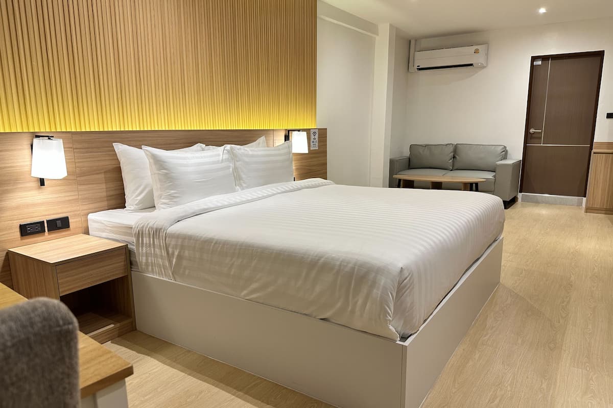 A modern hotel room with a large bed, bedside tables, a sofa, and a desk.