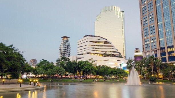 A cityscape with modern buildings, a central fountain, and a park with trees and people. - Winston Hotel (Bangkok)