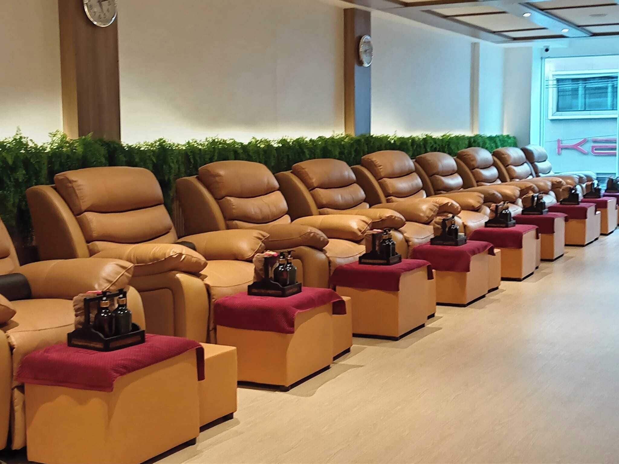 Une rangée de fauteuils de massage dotés de repose-pieds et une petite table avec une bouteille sur chaque fauteuil.
