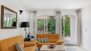 Een woonkamer met een bank, een salontafel, een lamp en een groot raam met gordijnen.
