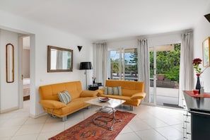 Una sala de estar con dos sofás, una mesa de centro, una lámpara y vistas al exterior con vegetación.