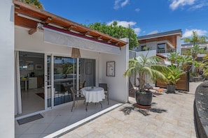 Una casa moderna con un patio, puertas corredizas de vidrio, una zona de comedor y plantas en macetas.