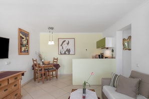A living room with a sofa, a dining table with chairs, a TV, and a kitchen area in the background. - Vacation Home 'Bianca Cactus' with Sea View, Private Terrace and Wi-Fi (Las Breñas)