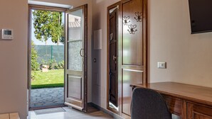 An open sliding glass door leading to a garden, a wooden desk, and a chair.