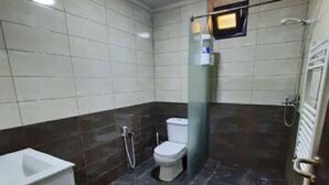 Un baño con inodoro blanco, lavamanos blanco y zona de ducha.