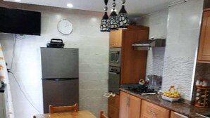 Una cocina con armarios de madera, un refrigerador de acero inoxidable, una mesa de comedor de madera con sillas y una lámpara colgante.