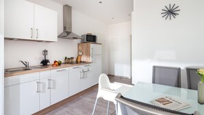 A modern kitchen with white cabinets, a microwave, and a dining area with a glass table and chairs. - // KING APARTMENTS - APARTMENT 2 // (Norderney)