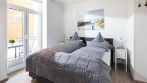 A bedroom with a large bed, a nightstand, a wall-mounted lamp, and a window with a view of a brick building. - // KING APARTMENTS - APARTMENT 2 // (Norderney)