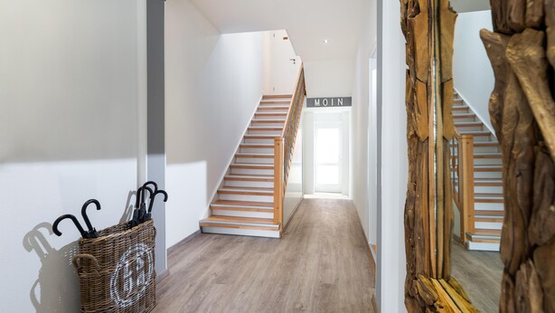 A hallway with a wooden staircase, a wicker basket with umbrellas, and a large mirror. - // KÖNIG APARTMENTS - APARTMENT 3 // (Norderney)