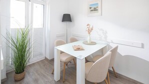 A modern dining area with a white table, beige chairs, a potted plant, and a wall-mounted lamp.