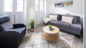 A modern living room with a grey sofa, a black leather chair, a round wooden coffee table, and a patterned rug.