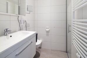 A modern bathroom with a white sink, mirror, and toilet. - // KÖNIG APARTMENTS - APARTMENT 3 // (Norderney)