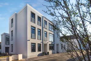 En moderne bygning med flere etager, en flad facade, store vinduer og et hvidt stakerværk foran.