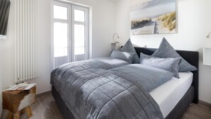 A bedroom with a bed, a bedside table, a lamp, and a window. - // KING APARTMENTS - APARTMENT 5 // (Norderney)