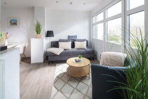 A modern living room with a grey sofa, a round coffee table, and a view of the outdoors through large windows. - // KING APARTMENTS - APARTMENT 6 // (Norderney)