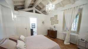 Une chambre avec un grand lit, un plancher en bois, une commode, un radiateur et un lustre.