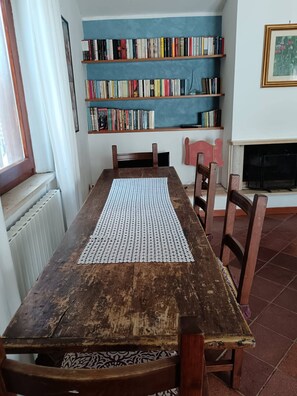 A wooden dining table with a placemat, surrounded by chairs, in a room with a bookshelf and a fireplace. - Poggio Bassotto, Your Peaceful Retreat Near the Heart of Rome (Sacrofano)