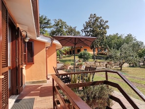 A patio with a table and chairs, a wooden railing, and a view of a garden and buildings in the background. - Poggio Bassotto, Your Peaceful Retreat Near the Heart of Rome (Sacrofano)