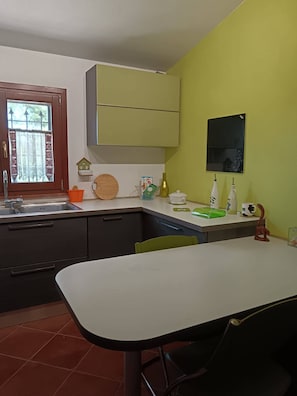 A kitchen with a dining table, cabinets, and a window with a curtain.