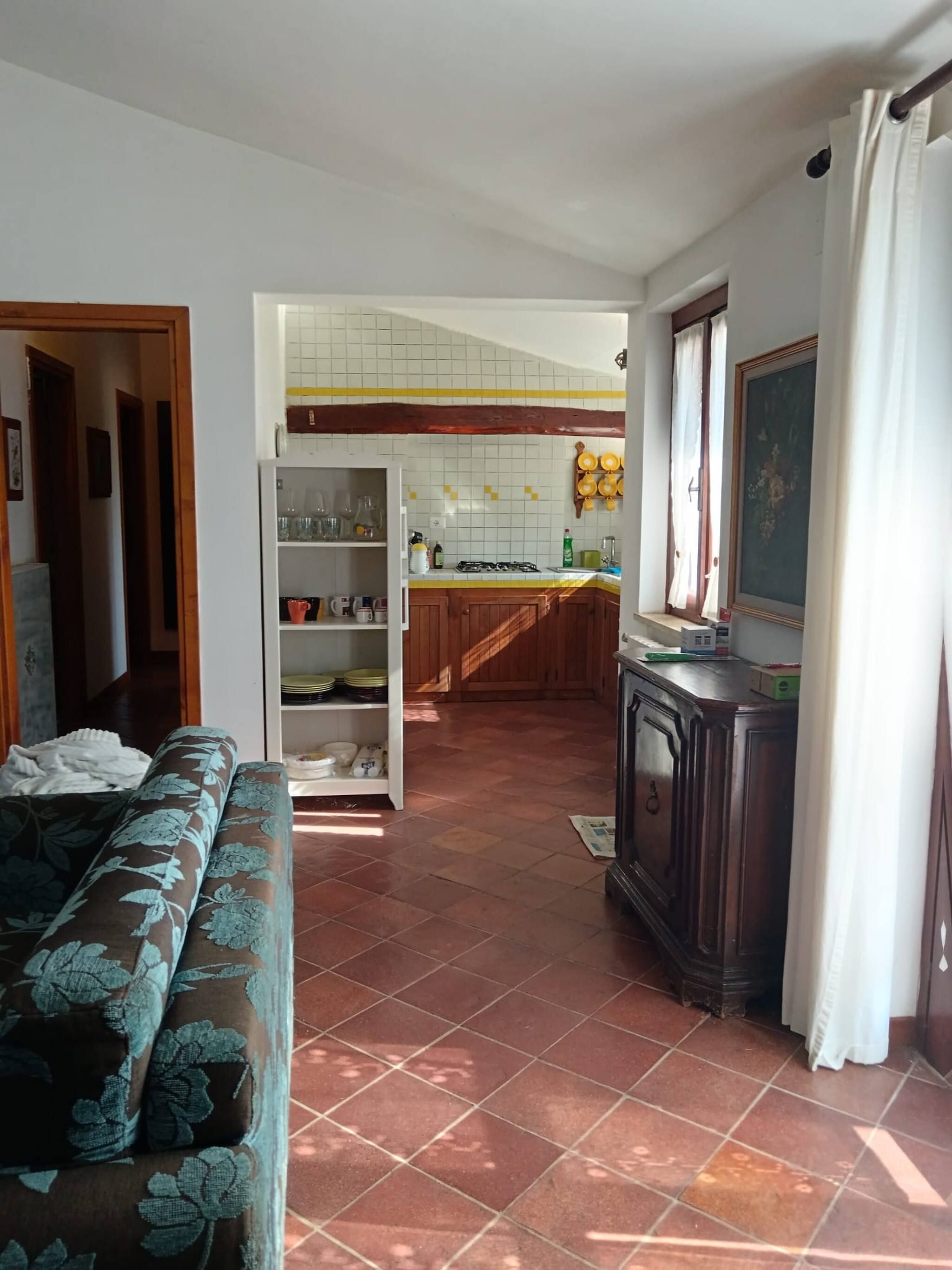 A spacious living room with a sofa, a kitchen area with wooden cabinets, and a tiled floor.
