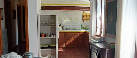 A spacious living room with a sofa, a kitchen area with wooden cabinets, and a tiled floor.