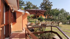 A patio with a table and chairs, a wooden railing, and a view of a garden and buildings in the background. - Poggio Bassotto, Your Peaceful Retreat Near the Heart of Rome (Sacrofano)