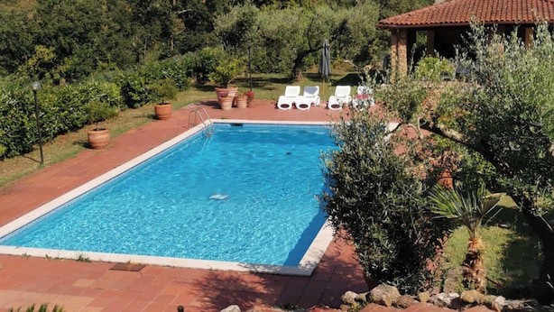 A rectangular swimming pool with a clear blue water surface, surrounded by a red tiled deck. There are white lounge chairs and a small gazebo with a tiled roof in the background. - Poggio Bassotto, Your Peaceful Retreat Near the Heart of Rome (Sacrofano)