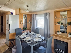 A dining area with a table set for six, a refrigerator, a mirror, and shelves with plants.