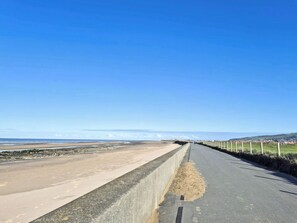 A coastal road with a concrete barrier, a sandy beach, and a clear blue sky.