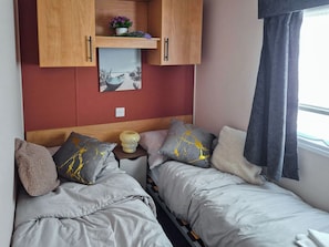 Une chambre avec deux lits, une étagère en bois ornée d’un tableau et une fenêtre avec des rideaux.
