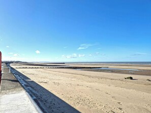 A beach with a concrete walkway, a wooden pier, and a distant view of the sea.