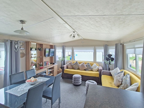A living area with a sofa, TV, dining table, chairs, and a ceiling fan.