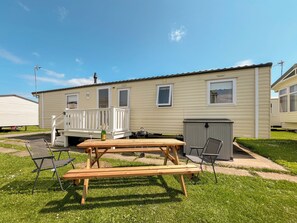 A mobile home with a deck, a picnic table, and a grill.
