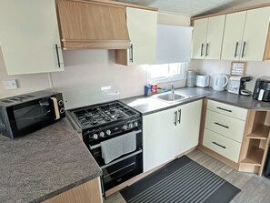 A compact kitchen with a gas stove, microwave, sink, and wooden cabinets. - 3 bedroom accommodation in Rhyl, near Towyn (Rhyl, near Towyn)
