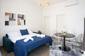 Une chambre d’hôtel moderne, équipée d’un lit, d’une table à manger avec des chaises et d’œuvres d’art abstraites accrochées au mur.