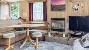 A cozy room with a sofa, a round table, a TV, a fireplace, and a window with curtains. - 3 bedroom accommodation in Tosside, near Settle (Tosside, near Settle)