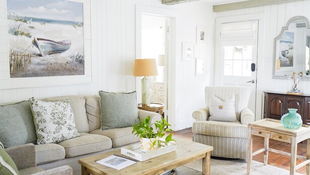 Una sala de estar acogedora con sofá, sillón, mesa de centro y un cuadro con una playa.