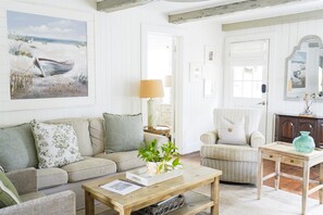 Un salon chaleureux avec un canapé, un fauteuil, une table basse et un tableau représentant une scène de plage.