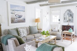 A cozy living room with a sofa, armchairs, a coffee table, and a painting of a beach scene. - Beachside Charm – Walk to Sand & Village Pier (St Simons Island)