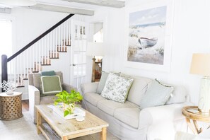 A living room with a staircase, a sofa, a coffee table with a plant, and a painting on the wall. - Beachside Charm – Walk to Sand & Village Pier (St Simons Island)