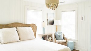 Un dormitorio con una cama grande, una silla de mimbre, una mesita de noche y una lámpara colgante.
