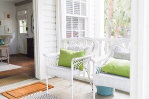 A white wicker chair with a green cushion on a porch. - Beachside Charm – Walk to Sand & Village Pier (St Simons Island)