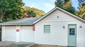 A small, single-story building with a garage door and a green door, surrounded by trees. - Cozy Studio Steps from Beach & Pier Village! (St Simons Island)
