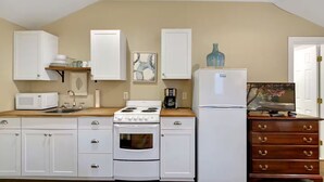 A kitchen with white cabinets, a stove, a microwave, a refrigerator, and a wooden countertop. - Cozy Studio Steps from Beach & Pier Village! (St Simons Island)