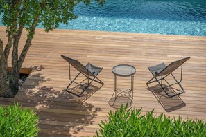 A wooden deck with two lounge chairs and a small round table, overlooking a clear blue pool. - Villa Les Santons - Sea view, private pool and quiet in Fréjus (Fréjus)