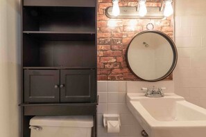 Een badkamer met een zwart kastje, een ronde spiegel, een witte wastafel en een toilet.