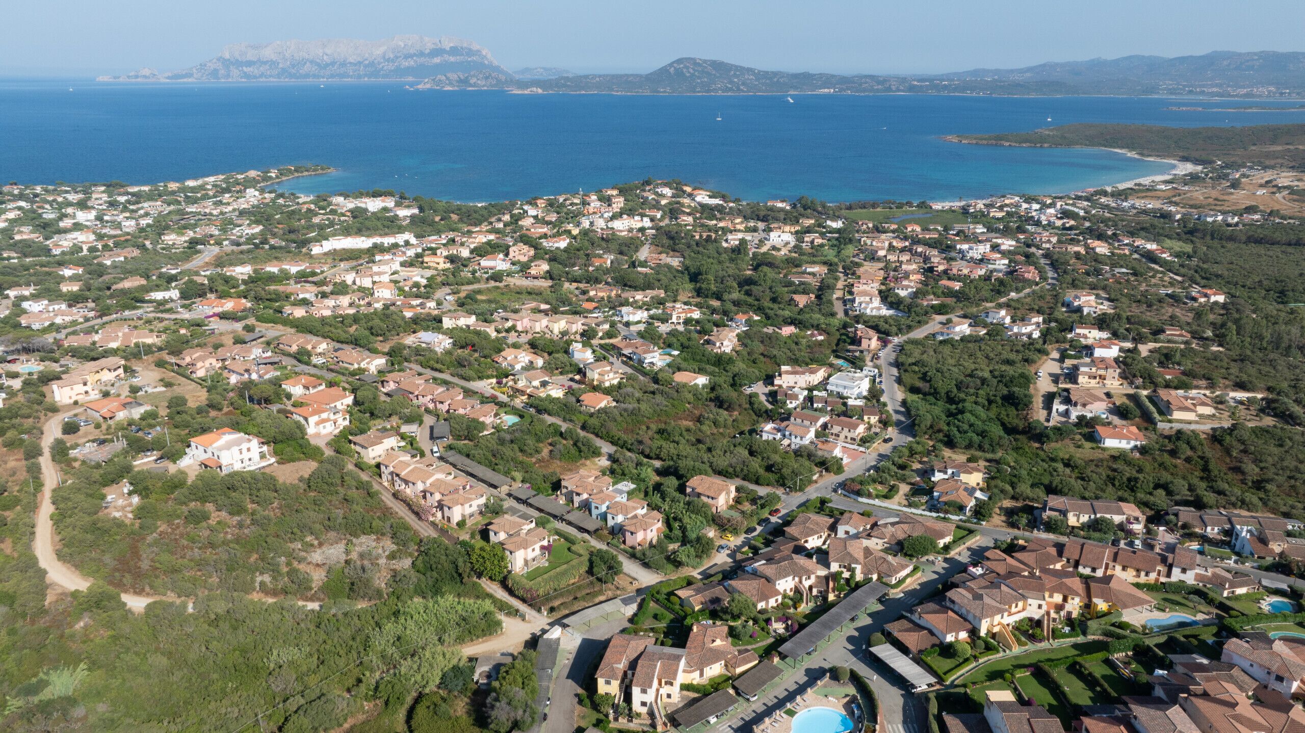An aerial view of a coastal residential area with houses, roads, and a clear view of the sea.